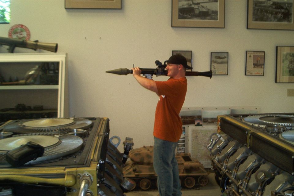 Man with rocket launcher in museum with tank models and engine parts