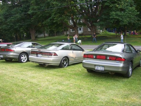 1996 Ford Probe - Three Ford Probes are lined up on a grassy lawn with trees and a house in the background.