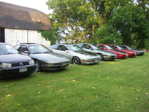 1996 Ford Probe - A collection of Ford Probes and a Volkswagen Golf are lined up on a grassy area next to a barn.