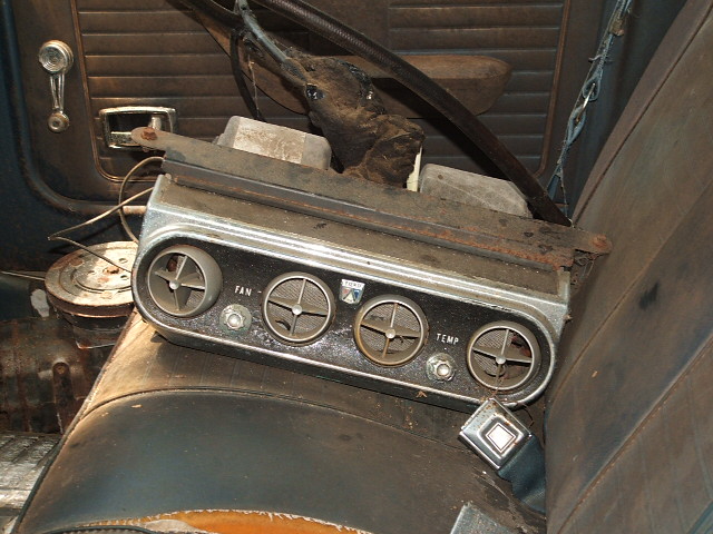 Aftermarket AC unit with four vents and fan/temp controls, resting on a worn car seat