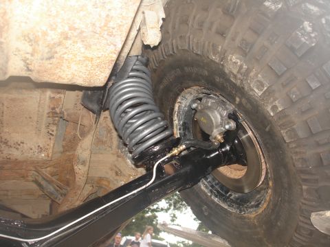 1987 Ford Bronco - The underside of an off-road vehicle shows its suspension components, including a large coil spring and brake assembly.