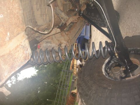 1987 Ford Bronco - Close-up of the suspension system and tire from beneath a vehicle.