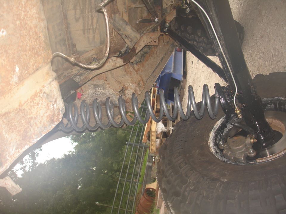 Front coil spring at full droop with black-painted radius arm, axle and brake line under a lifted truck