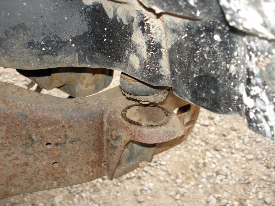 Close-up of rusty axle housing contacting a black bump stop under a truck on gravel