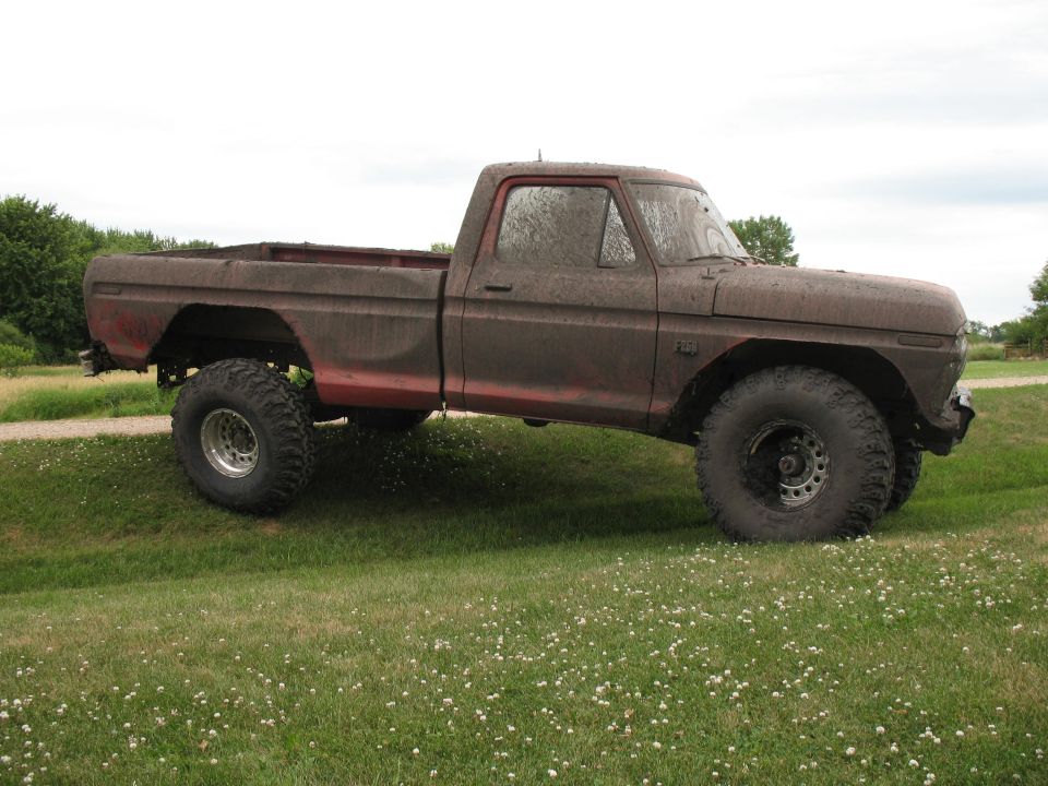 muddy 1973 Ford F-250 pickup truck with large tires parked on a grassy hill