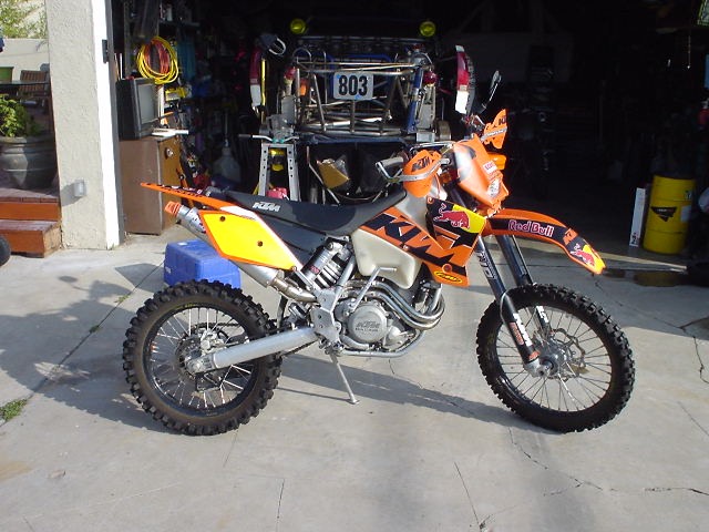 Orange KTM dual-sport dirt bike with Red Bull fork decals parked outside a garage