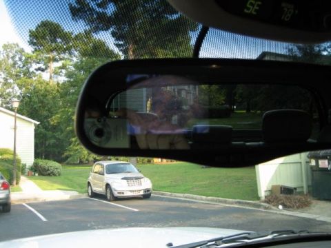 1986 Ford F-150 - A silver Chrysler PT Cruiser is parked in a lot, viewed through the windshield and side mirror.