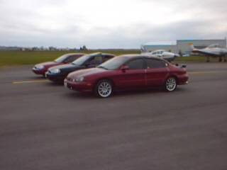 1998 Ford Taurus - Three sedans are parked on an asphalt surface, with airplanes visible in the background.