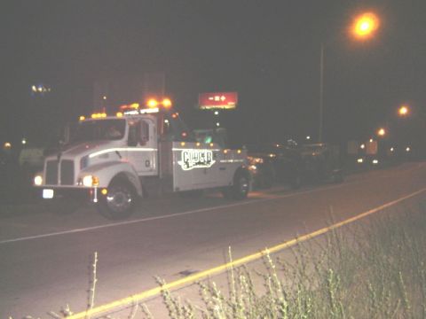 1992 Ford Bronco - A tow truck transports a vehicle on a highway at night.