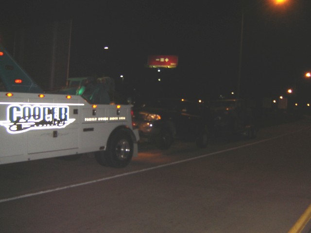 Tow truck with 'COOGLE' logo, dark SUV behind it at night