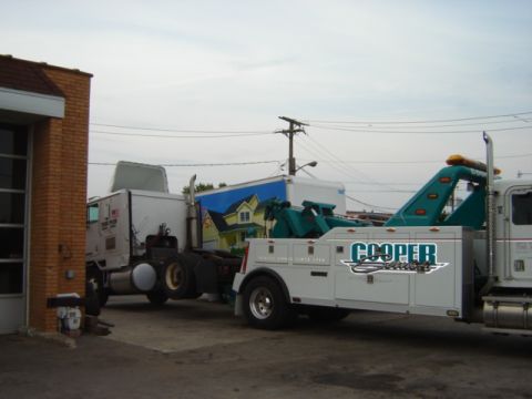 1992 Ford Bronco - A tow truck is parked next to a brick building with a mural on a trailer behind it.