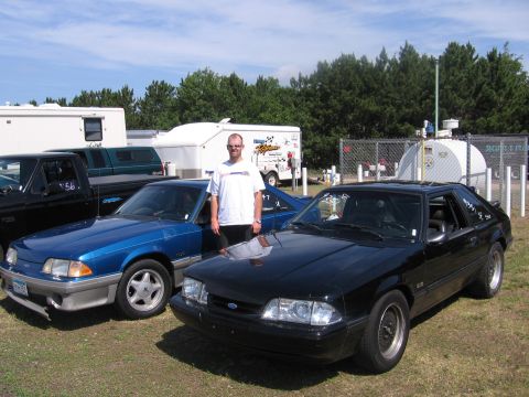 1989 Ford Mustang - Two Ford Mustangs are parked on grass with a man standing between them.