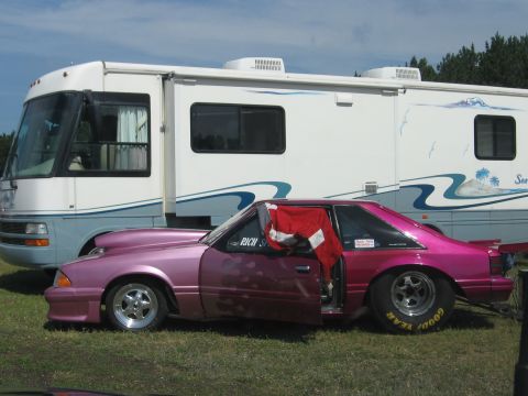 1989 Ford Mustang - A customized 1989 Ford Mustang with racing slicks and an open door sits parked in front of an RV.