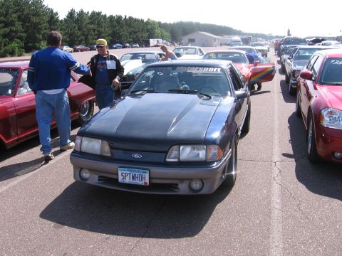 1989 Ford Mustang - A dark blue Ford Mustang is parked in a line of vehicles at what appears to be a race track or car show.