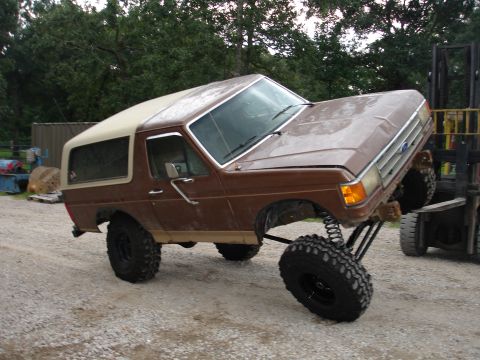 1987 Ford Bronco - A brown Ford Bronco is being lifted by a forklift, showing its modified suspension and large tires.