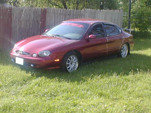 1998 Ford Taurus - A maroon sedan is parked on a grassy lawn next to a wooden fence.