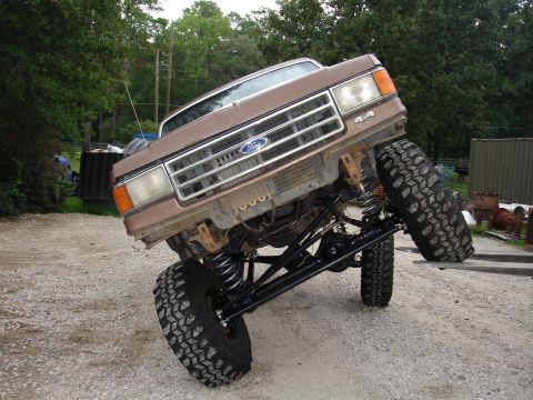 1987 Ford Bronco - This modified Ford F-Series truck displays a lifted suspension and oversized tires, with a visible '4x4' badge.