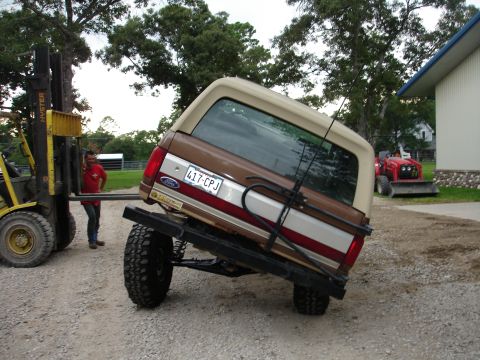 1987 Ford Bronco - Forklift lifting a 1987 Ford Bronco. A red tractor is visible in the background.