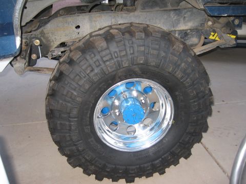 1990 Ford Bronco - A close-up view of a vehicle's wheel and suspension system, with a large tire and custom rim.