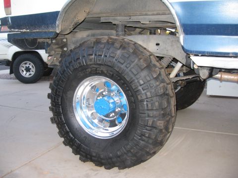 1990 Ford Bronco - Modified truck wheel and suspension detail, with another vehicle in the background.