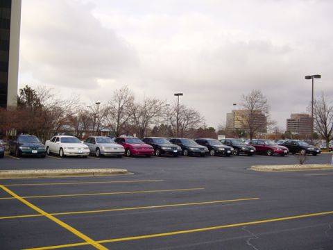1998 Ford Taurus - Several sedans are parked in a lot under an overcast sky, with a prominent red 1998 Ford Taurus among them.