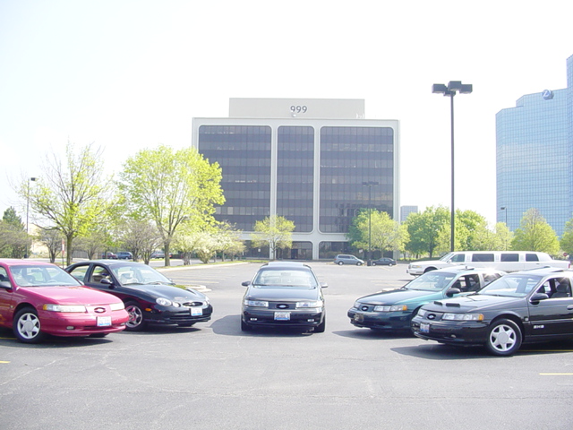 Several Ford Tauruses parked in a lot, with office buildings in the background