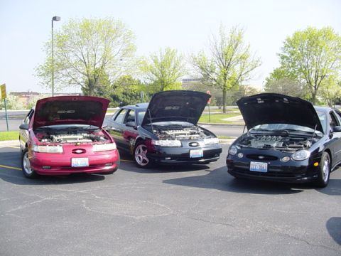 1998 Ford Taurus - Three Ford Taurus sedans, likely from the mid-1990s, are lined up with their hoods open in a parking lot.