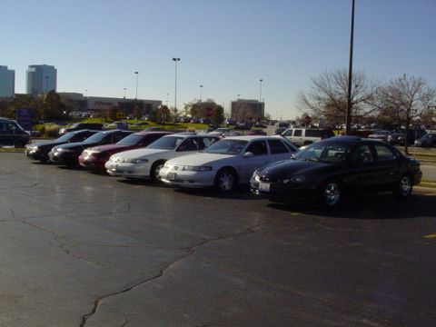 1998 Ford Taurus - A row of cars are parked in a lot with buildings in the background under a clear sky.