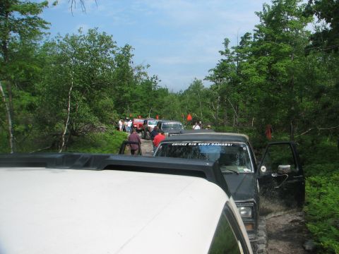 1992 Ford Bronco - A convoy of off-road vehicles navigates a muddy trail surrounded by dense foliage.