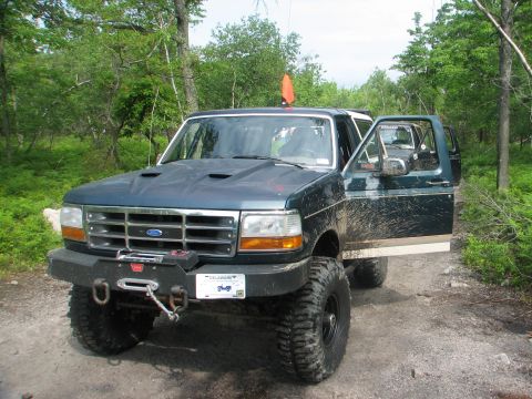 1992 Ford Bronco - Off-road modified 1992 Ford Bronco parked on a dirt path surrounded by trees.