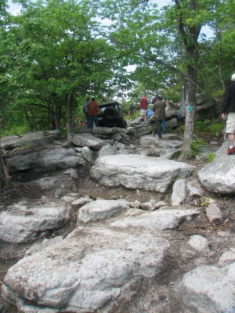 1992 Ford Bronco - Several people watch as an off-road vehicle attempts to climb a challenging rocky incline.