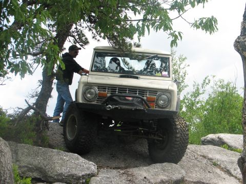 1992 Ford Bronco - A white Ford Bronco navigates a rocky terrain, with a person standing beside it.
