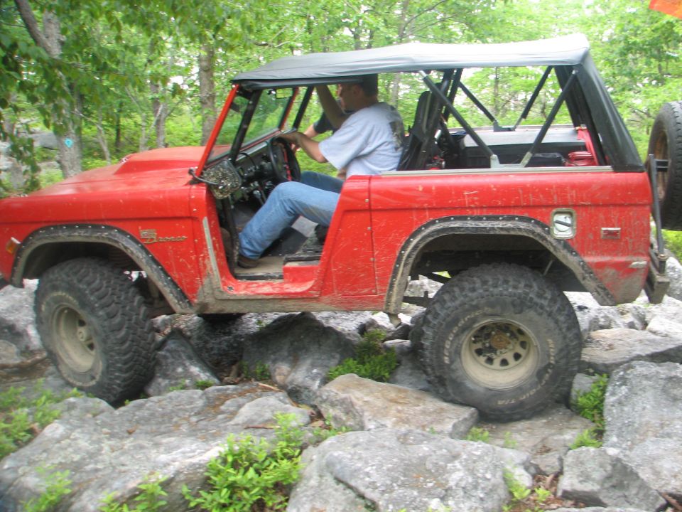 Red Ford Bronco driving over rocks on a trail. Driver is wearing jeans and a t-shirt