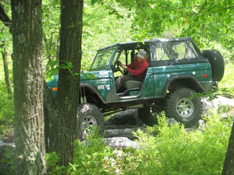 1992 Ford Bronco - A driver navigates a green Ford Bronco over a rocky path in a forest setting.