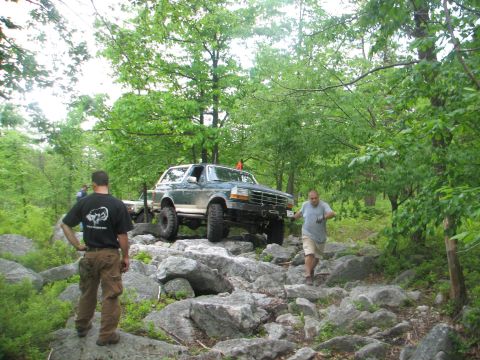1992 Ford Bronco - A 1992 Ford Bronco tackles a challenging rocky terrain in a wooded area.