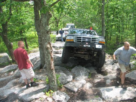 1992 Ford Bronco - A group of off-road vehicles traverse a challenging rocky path through a wooded area.