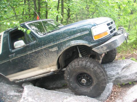 1992 Ford Bronco - A green 1992 Ford Bronco navigates a rocky trail, demonstrating its off-road capabilities.