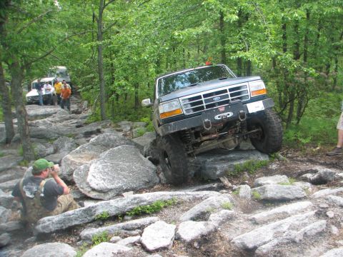 1992 Ford Bronco - A 1992 Ford Bronco tackles a challenging off-road course with other vehicles visible in the background.