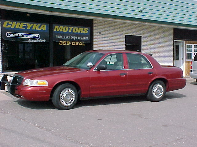 Dark red Ford Crown Victoria sedan parked outside Cheyka Motors dealership, side view