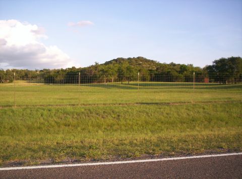 1986 Ford Bronco - A rural landscape features a grassy field, a wooded hill, and a fence line under a bright sky.