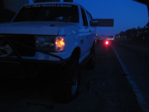 1990 Ford Bronco - white lifted truck at night showing a TheWebWheeler.com windshield banner, tubular front bumper, and round driving lights, with distant red…
