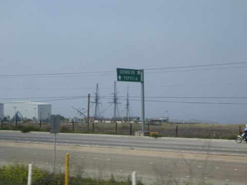 1990 Ford Bronco - green highway sign for ESTUDIOS FOX and Popotla points toward tall ship masts and a white film-studio building across an open field.