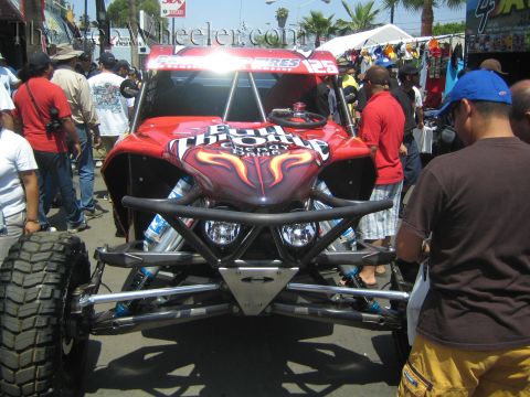 1990 Ford Bronco - red off-road race buggy with a flame-painted body and exposed tube front suspension is surrounded by spectators at a fair.