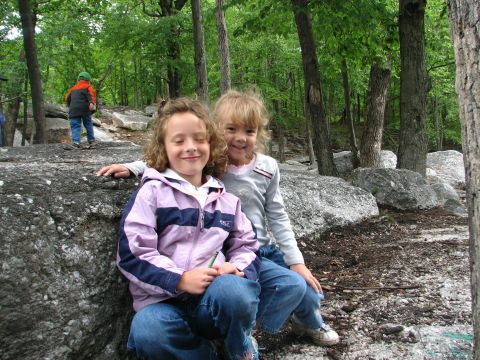 1992 Ford Bronco - Two smiling girls pose for a photo while sitting on large rocks in a wooded area with trees and foliage.