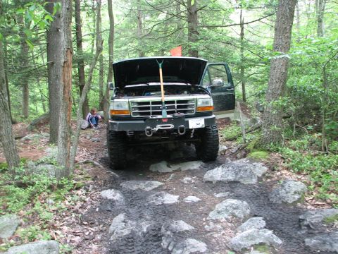1992 Ford Bronco - This Ford F-Series truck is navigating a challenging off-road trail with muddy terrain and large rocks.