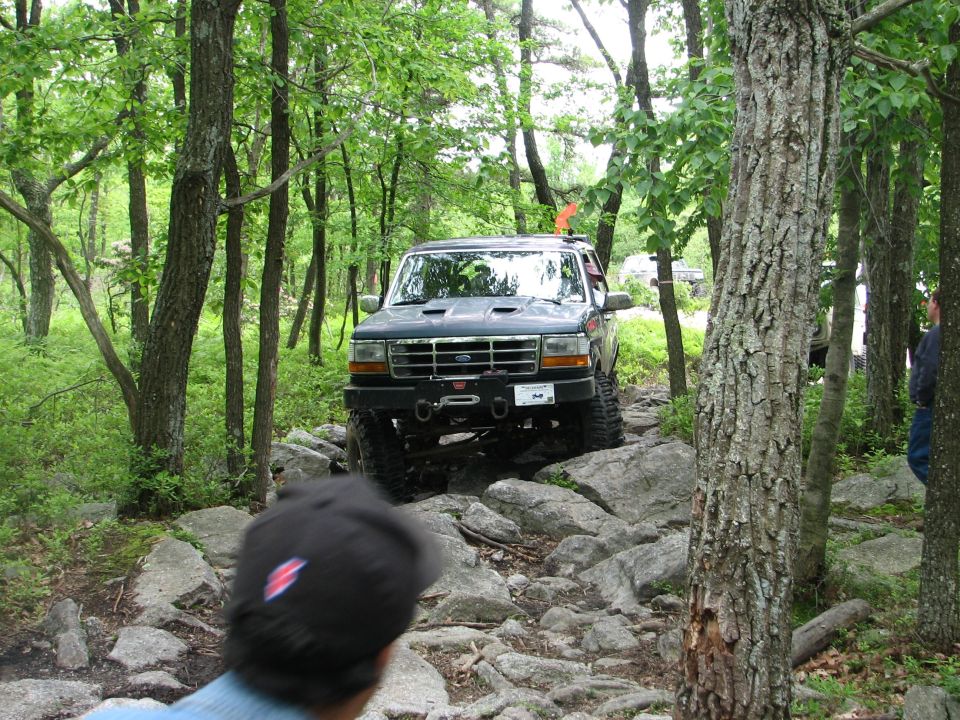 Lifted green Ford Bronco with winch bumper descending a rocky wooded trail