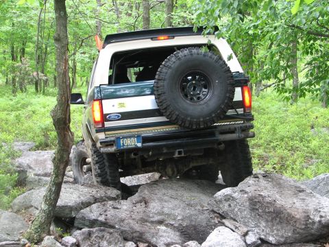 1992 Ford Bronco - A 1992 Ford Bronco navigates a rocky trail in a wooded area.