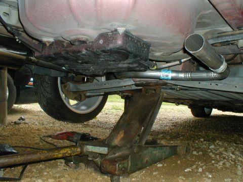 1998 Ford Taurus - The underside of a vehicle is visible, supported by a jack, with parts of the exhaust system and suspension clearly seen.