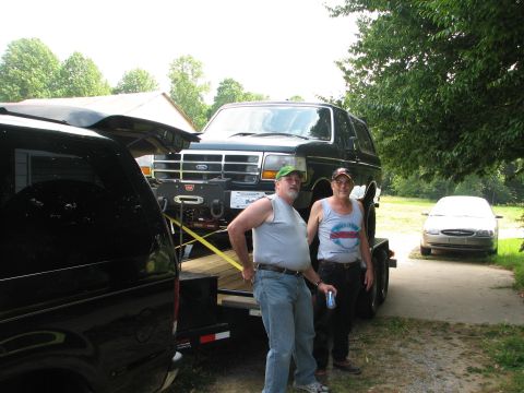 1992 Ford Bronco - Two men stand by a Ford Bronco being transported on a trailer, with another car visible in the background.