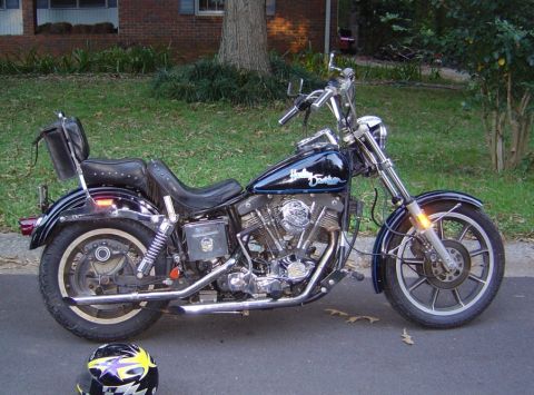 1986 Ford Bronco - A dark blue Harley-Davidson motorcycle is parked on the side of the road in front of a house.